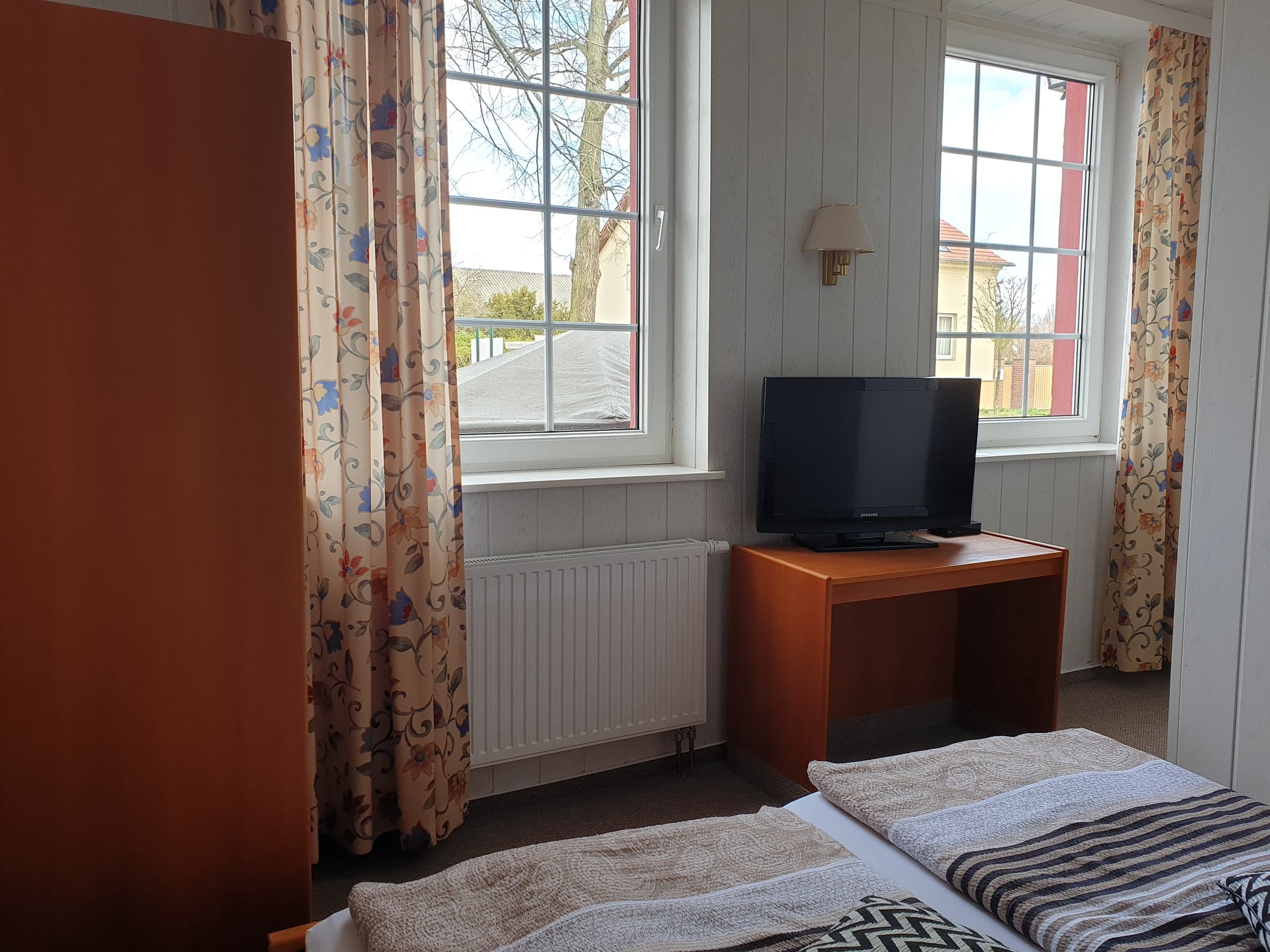 Doppelzimmer 1 mit Fernseher, Schreibtisch und zwei Fenstern